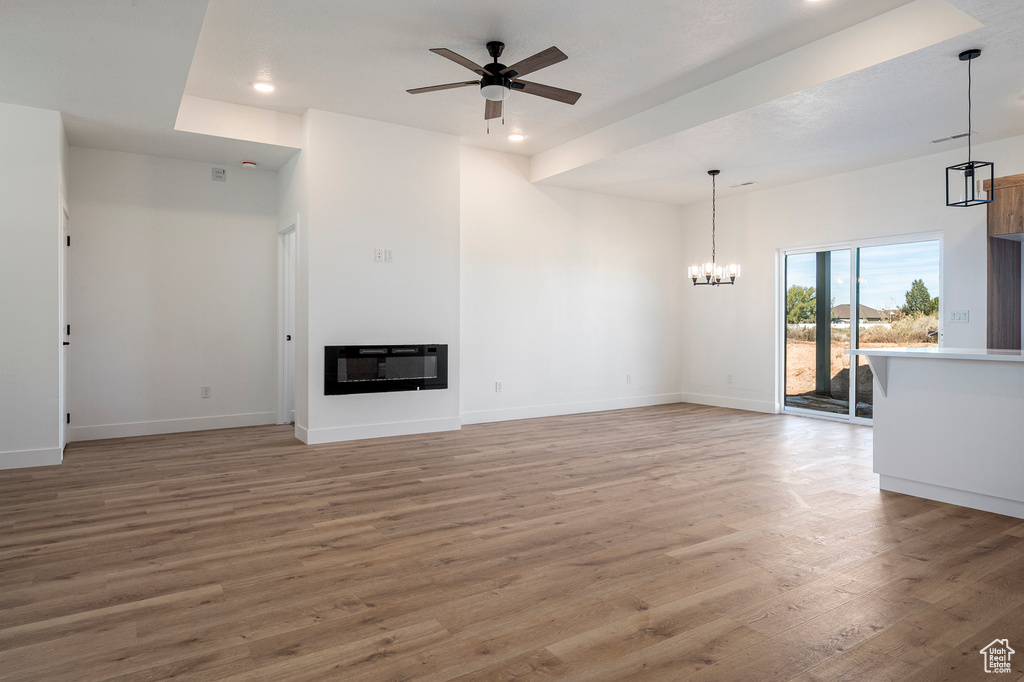 Unfurnished living room featuring heating unit, ceiling fan with notable chandelier, and hardwood / wood-style floors