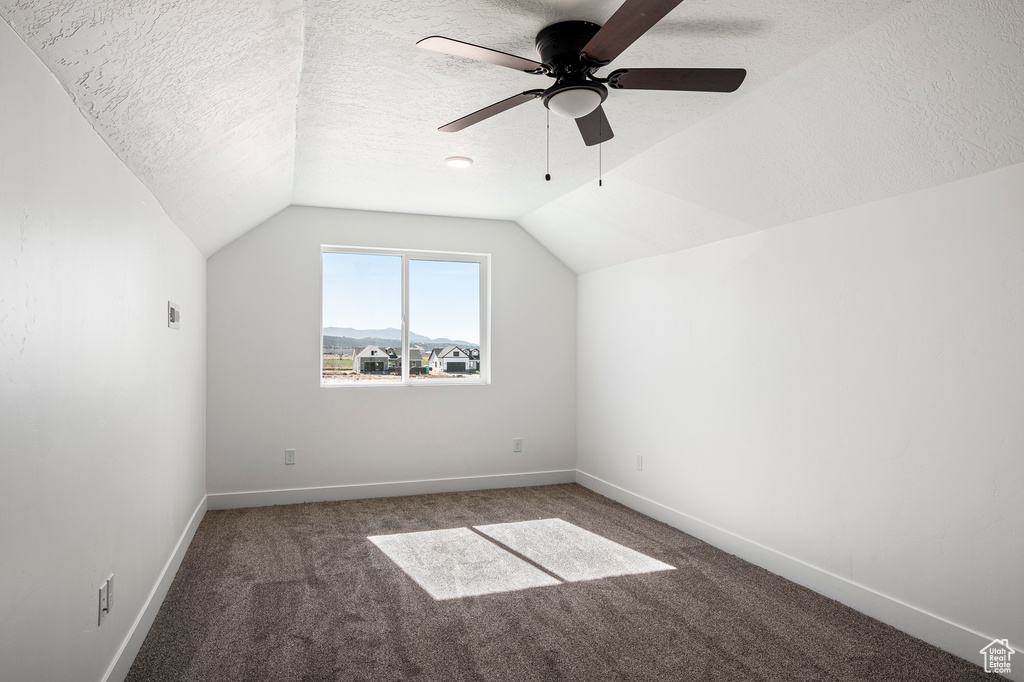 Bonus room with dark carpet, vaulted ceiling, a textured ceiling, and ceiling fan