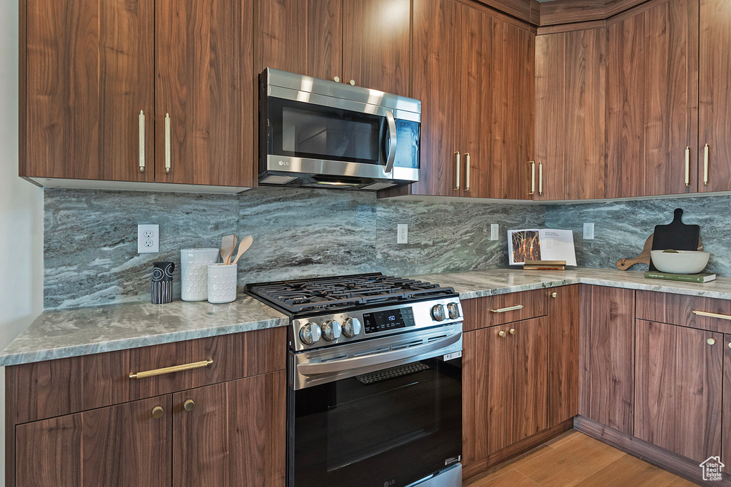 Kitchen with tasteful backsplash, appliances with stainless steel finishes, light hardwood / wood-style flooring, and light stone countertops