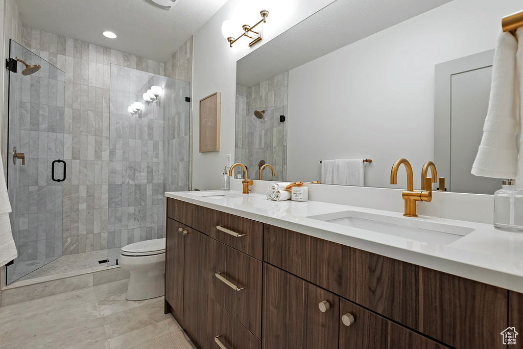 Bathroom featuring a shower with shower door, dual vanity, tile patterned flooring, and toilet