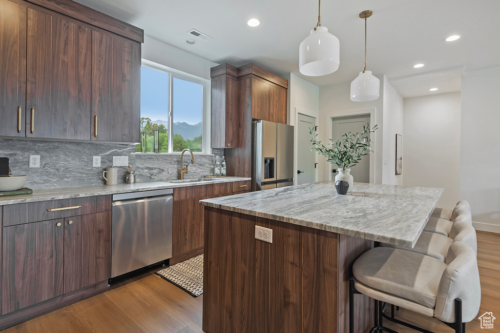 Kitchen featuring a breakfast bar, appliances with stainless steel finishes, hardwood / wood-style flooring, tasteful backsplash, and sink