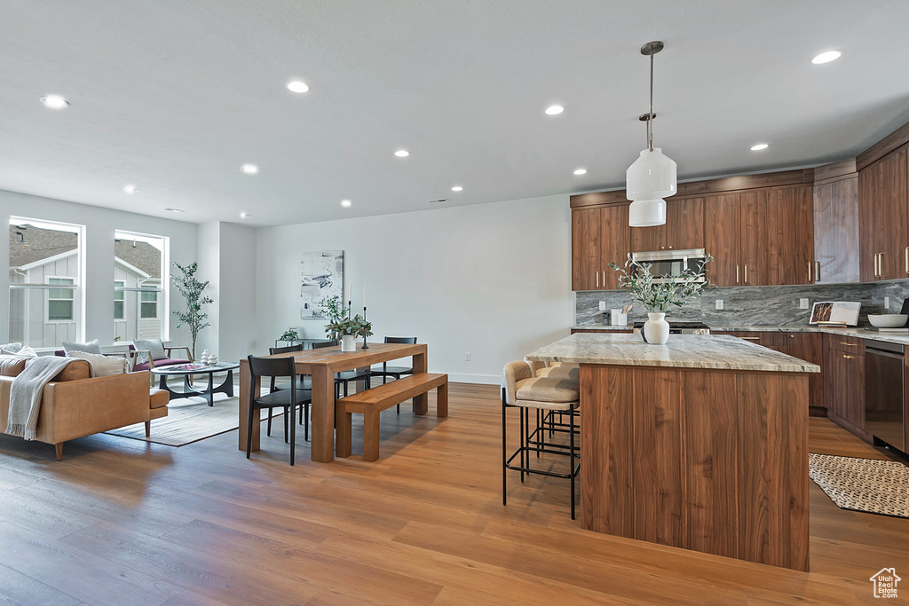 Kitchen with pendant lighting, hardwood / wood-style floors, a kitchen bar, a kitchen island, and backsplash