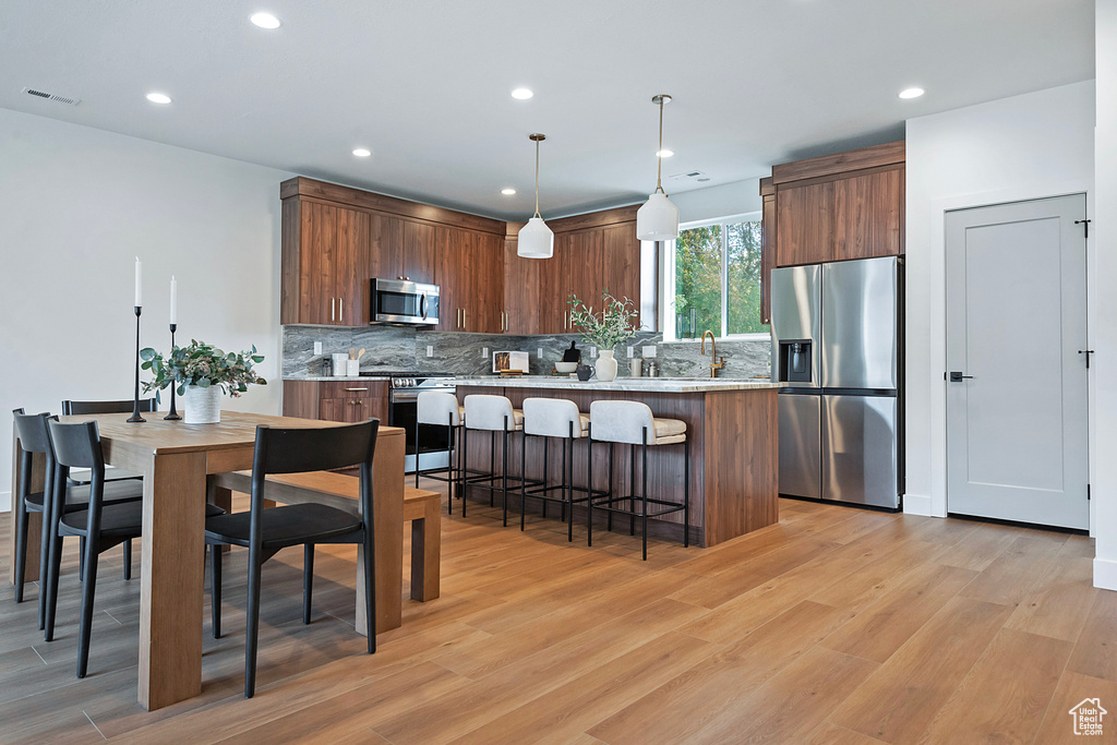 Kitchen featuring light wood-type flooring, stainless steel appliances, a kitchen bar, and decorative backsplash