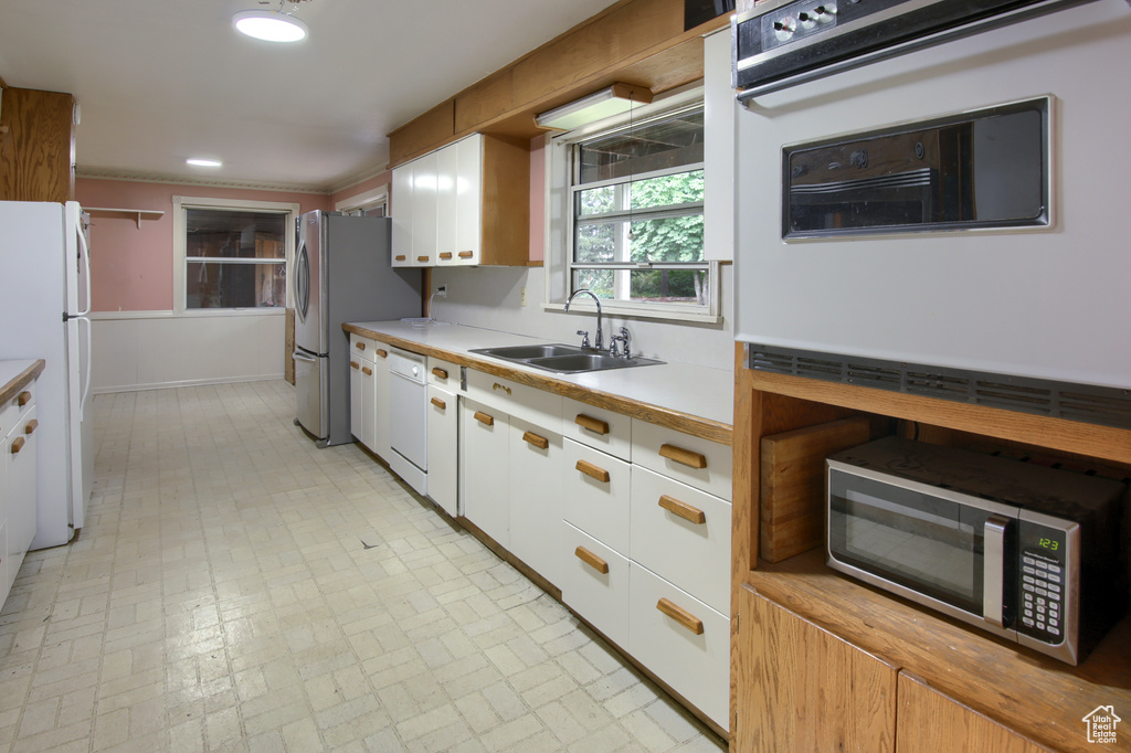 Kitchen with white cabinets, sink, white appliances, and light tile patterned floors