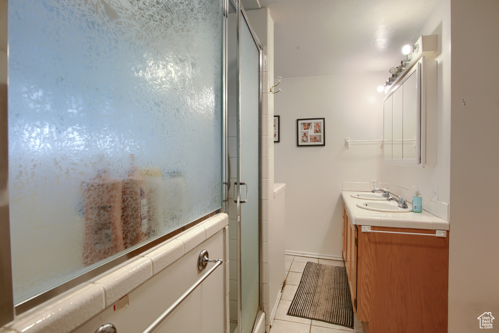 Bathroom featuring tile patterned floors, dual vanity, and an enclosed shower