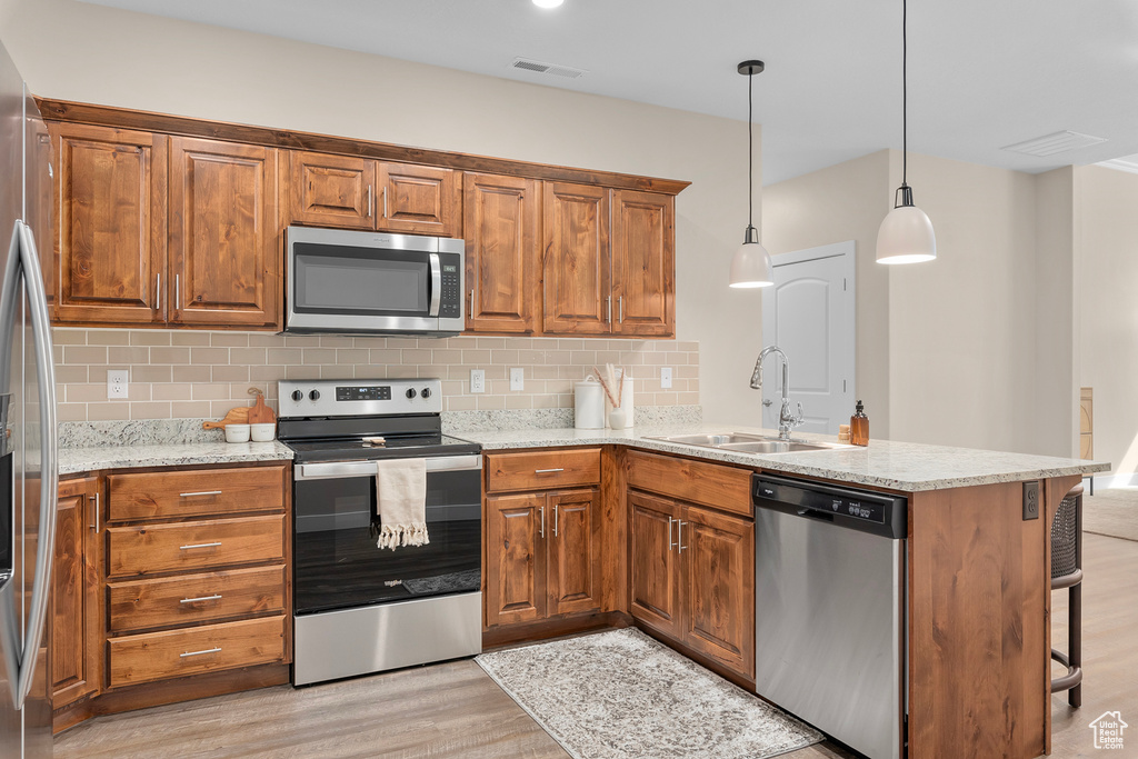 Kitchen featuring tasteful backsplash, appliances with stainless steel finishes, kitchen peninsula, and light hardwood / wood-style floors