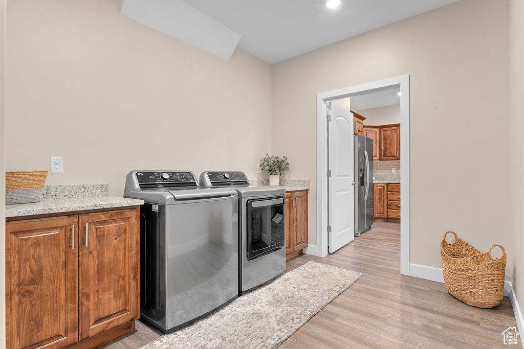 Washroom with cabinets, light wood-type flooring, and washing machine and clothes dryer