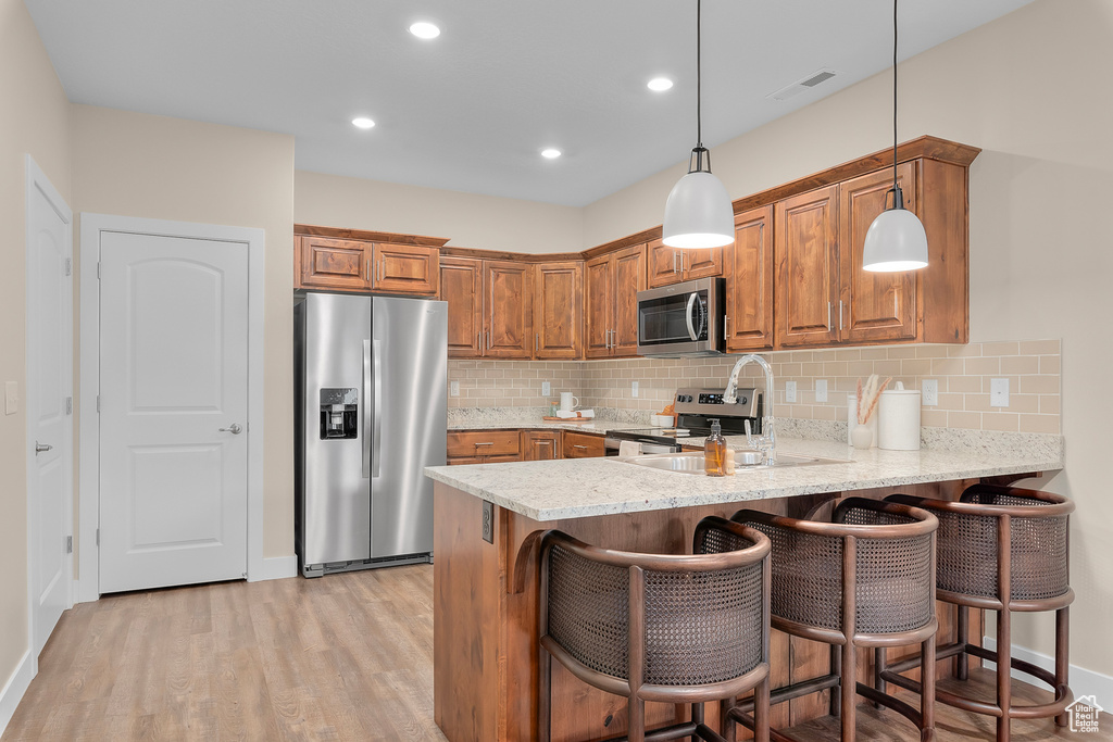 Kitchen featuring light wood-type flooring, stainless steel appliances, backsplash, a kitchen bar, and decorative light fixtures