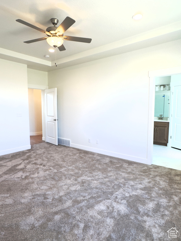 Empty room featuring ceiling fan, sink, a raised ceiling, and carpet