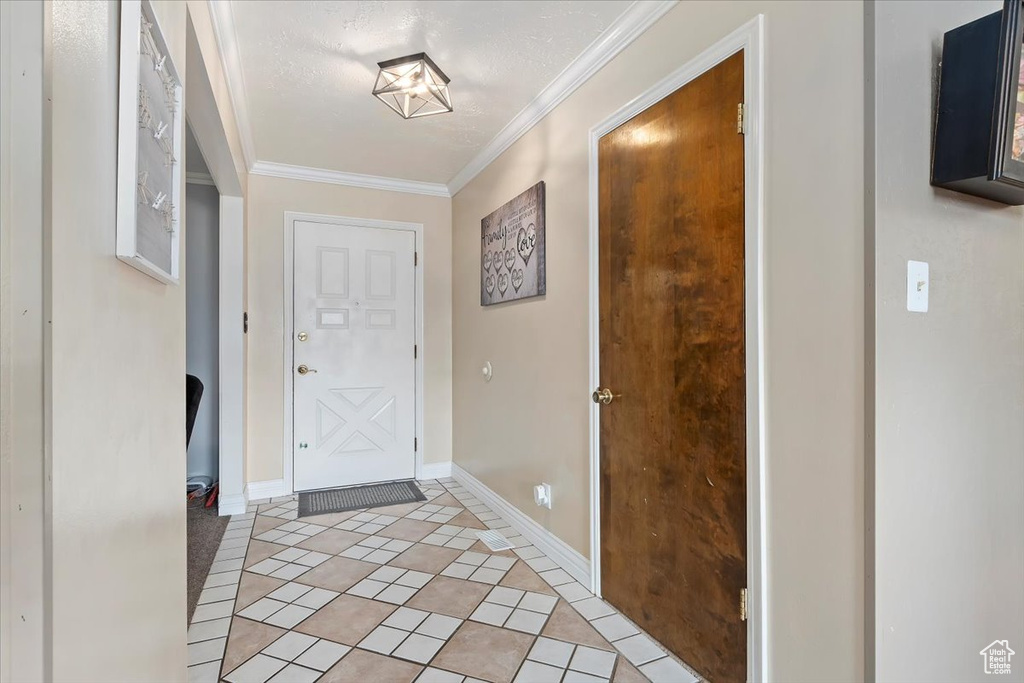 Foyer entrance with ornamental molding, a textured ceiling, and light tile patterned floors