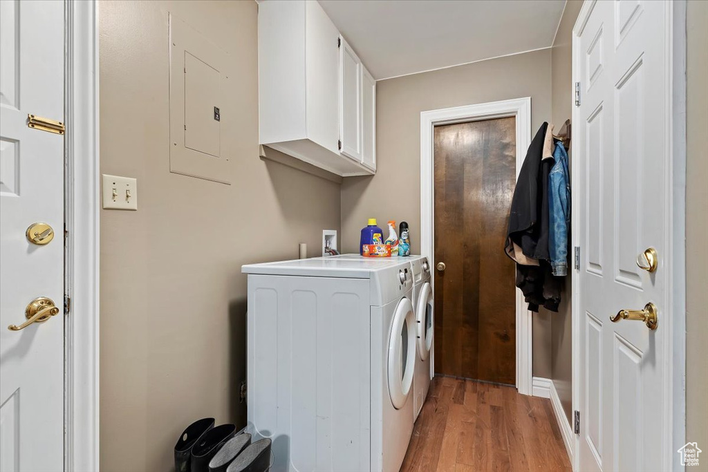 Laundry room featuring cabinets, light wood-type flooring, electric panel, and separate washer and dryer