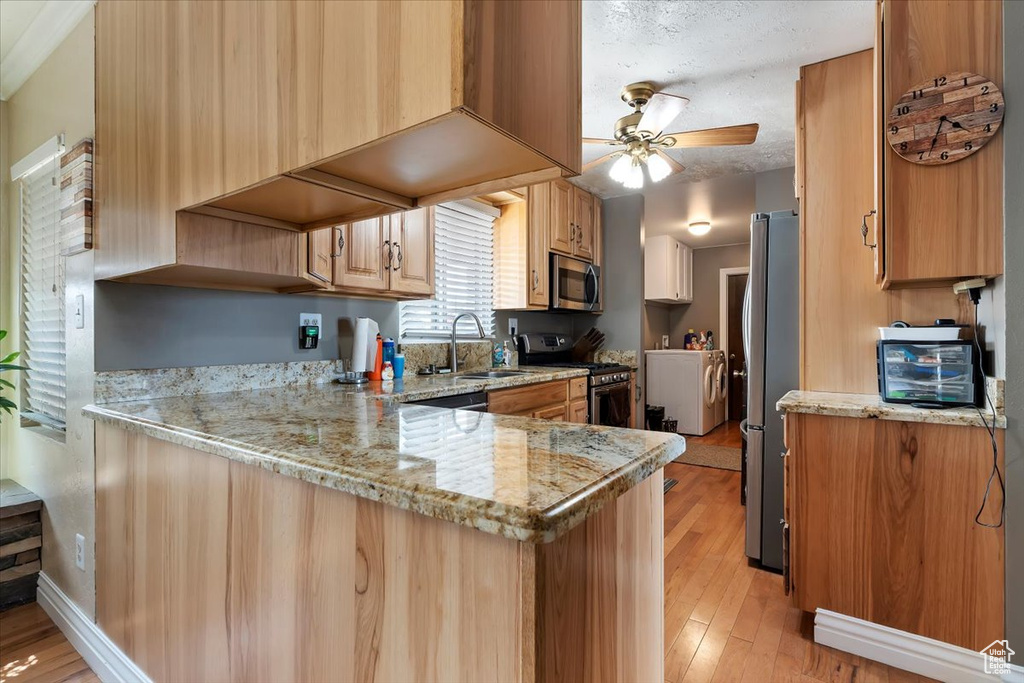 Kitchen with ceiling fan, kitchen peninsula, light stone countertops, light hardwood / wood-style floors, and stainless steel appliances