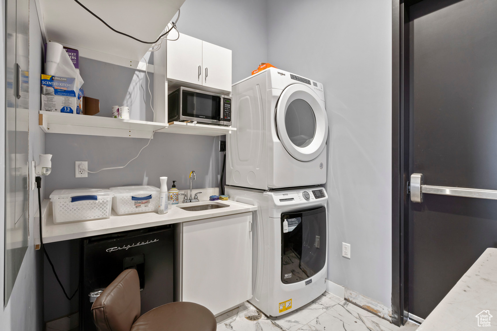 Laundry room with cabinets, light tile patterned flooring, stacked washing maching and dryer, and sink