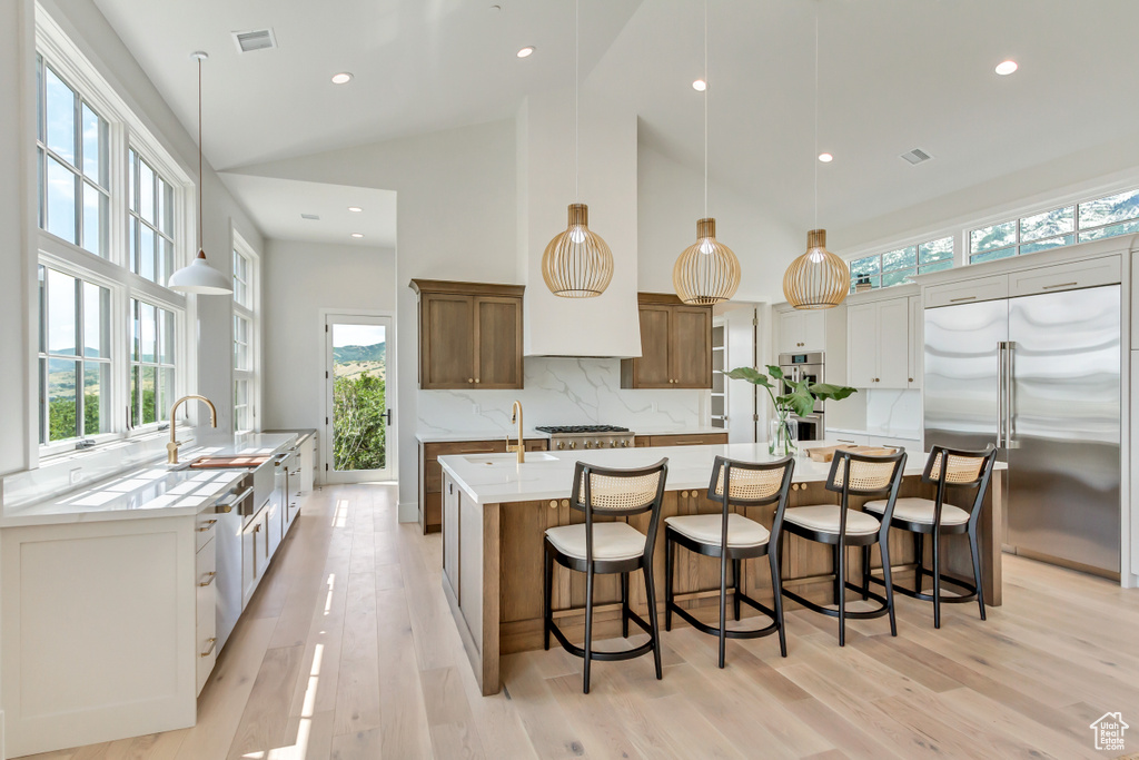 Kitchen with appliances with stainless steel finishes, a kitchen island with sink, decorative backsplash, and white cabinetry