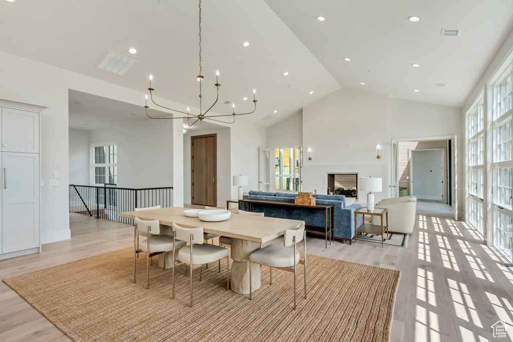 Dining space with high vaulted ceiling, light hardwood / wood-style flooring, a wealth of natural light, and an inviting chandelier