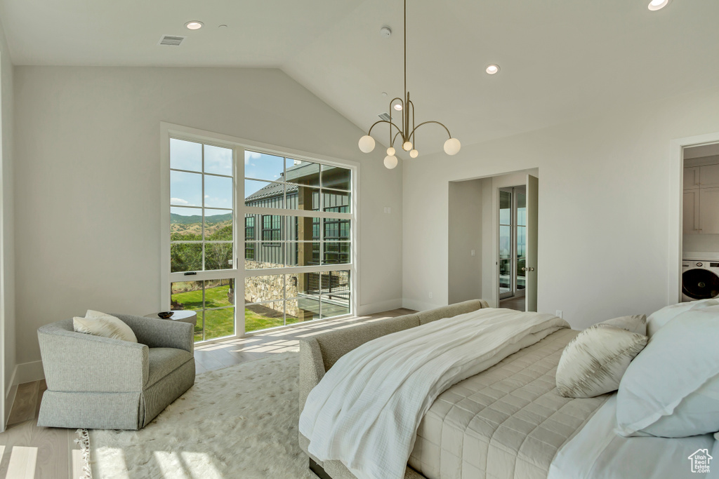 Bedroom with light wood-type flooring, washer / clothes dryer, lofted ceiling, and an inviting chandelier