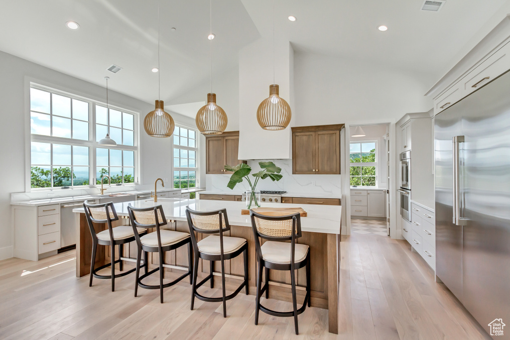 Kitchen with tasteful backsplash, a center island with sink, pendant lighting, stainless steel appliances, and light hardwood / wood-style flooring