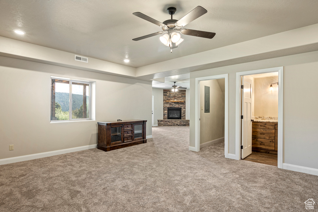 Carpeted spare room featuring a fireplace, electric panel, and ceiling fan