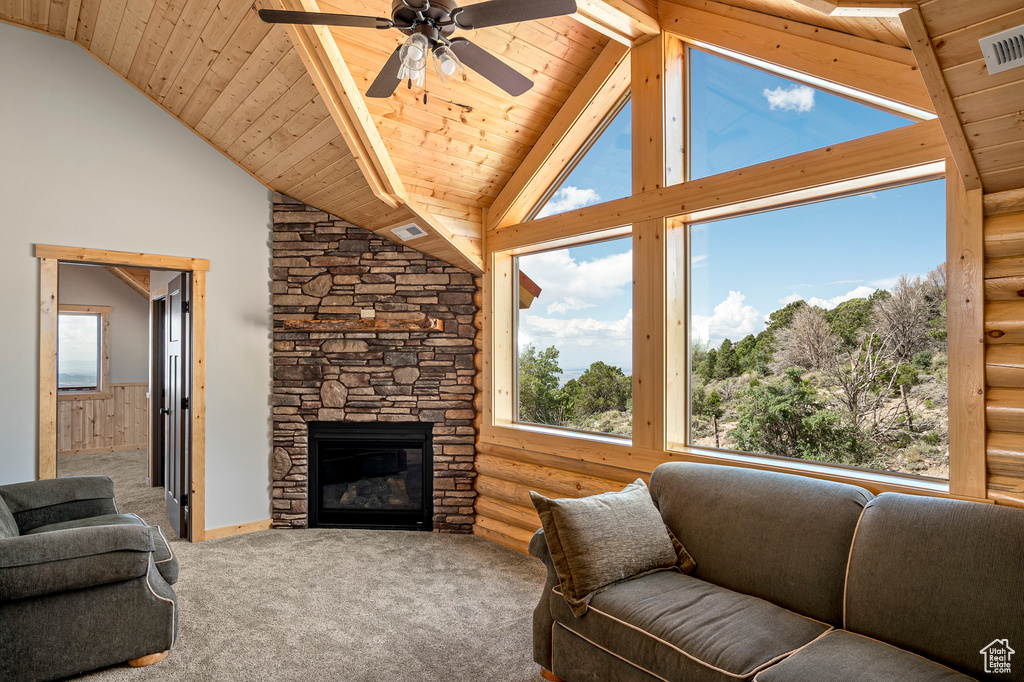 Carpeted living room featuring a stone fireplace, beam ceiling, rustic walls, ceiling fan, and wood ceiling