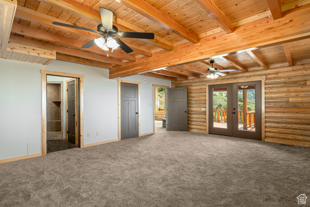 Carpeted empty room with rustic walls, french doors, beamed ceiling, and wood ceiling