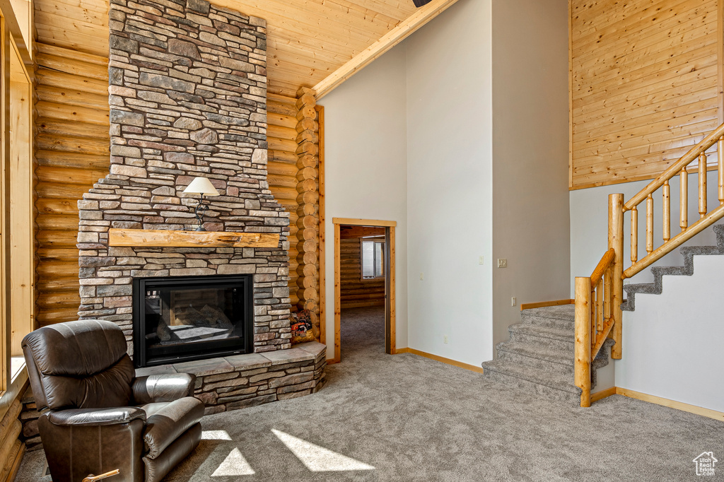 Carpeted living room featuring rustic walls, high vaulted ceiling, a stone fireplace, and wood ceiling