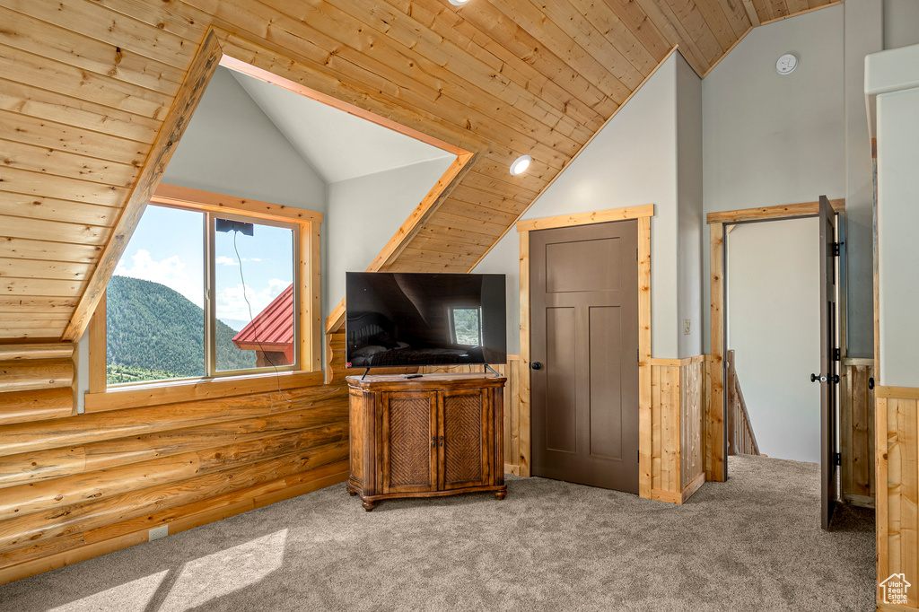 Interior space with rustic walls, carpet flooring, vaulted ceiling, and wooden ceiling