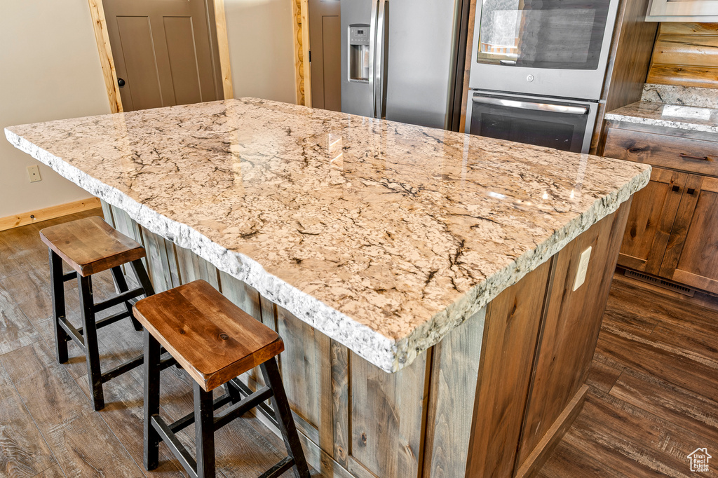 Kitchen featuring dark hardwood / wood-style floors, stainless steel appliances, a kitchen breakfast bar, and light stone countertops