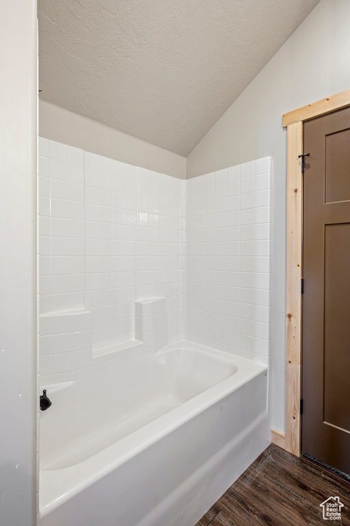 Bathroom featuring wood-type flooring, a textured ceiling, vaulted ceiling, and bathtub / shower combination