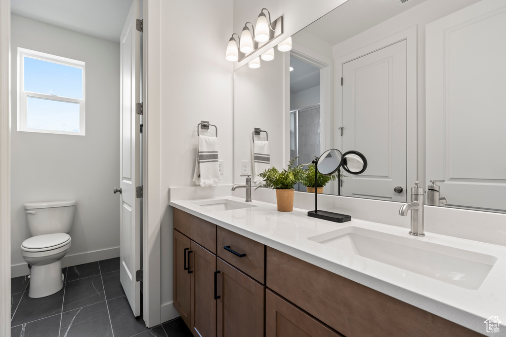 Bathroom featuring double sink vanity, tile patterned flooring, and toilet