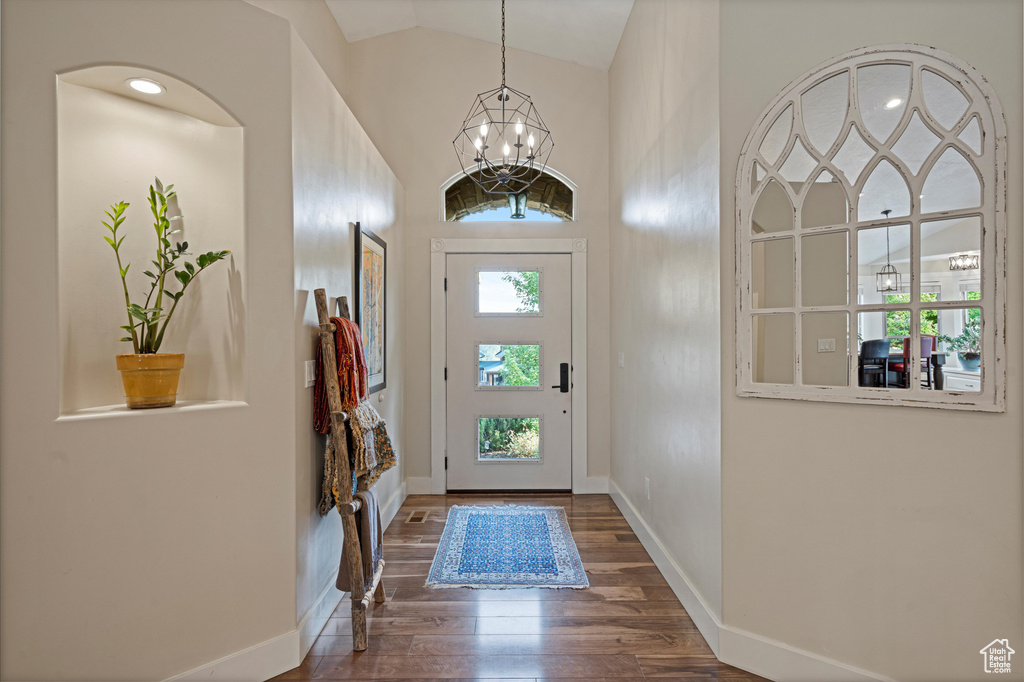 Foyer with dark wood-type flooring, lofted ceiling, and an inviting chandelier