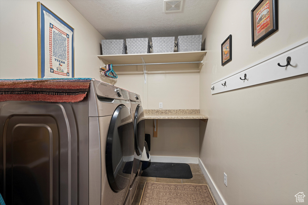 Clothes washing area with independent washer and dryer, tile patterned floors, and a textured ceiling