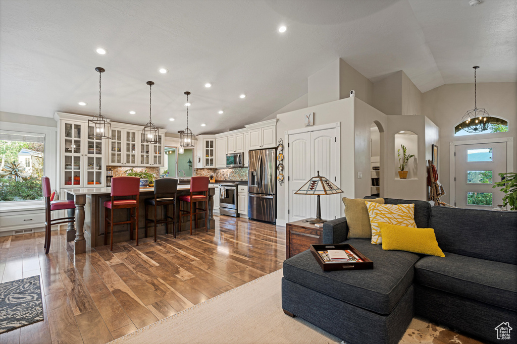 Living room featuring sink, high vaulted ceiling, wood-type flooring, and an inviting chandelier