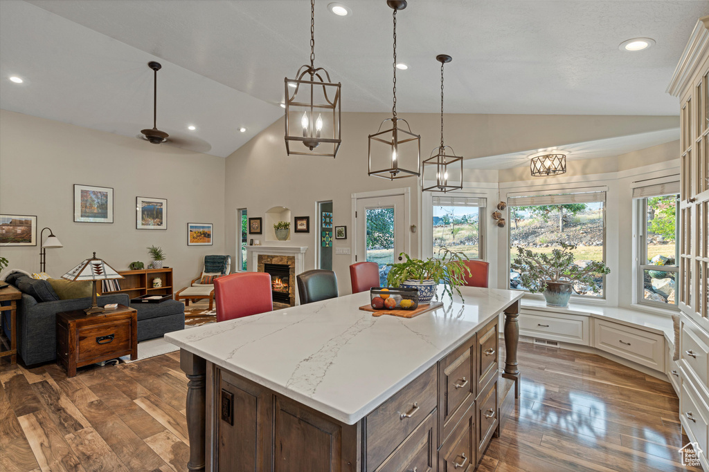 Kitchen with light stone counters, vaulted ceiling, a kitchen island, hardwood / wood-style flooring, and decorative light fixtures