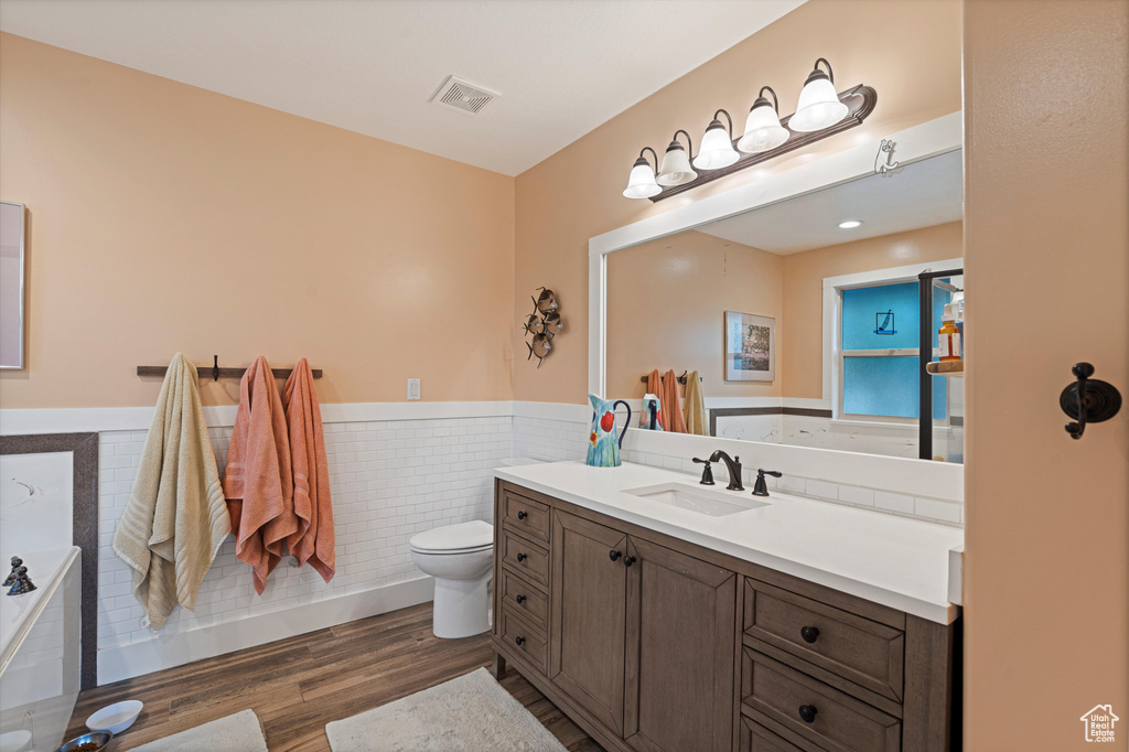 Bathroom featuring a bathtub, toilet, tile walls, vanity, and wood-type flooring