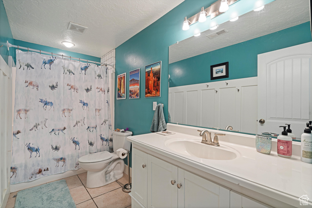 Bathroom featuring a textured ceiling, toilet, vanity, and tile patterned flooring