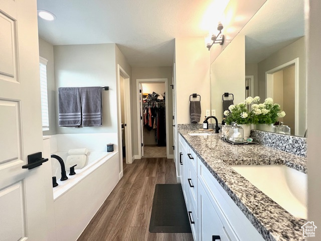 Bathroom featuring double sink vanity, a relaxing tiled tub, and wood-type flooring