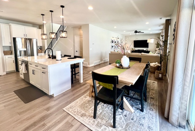 Kitchen with light wood-type flooring, a center island with sink, white cabinetry, and decorative light fixtures