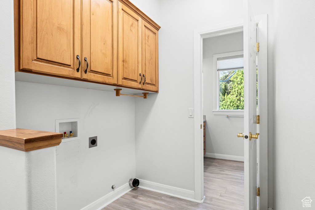 Laundry room with hookup for a washing machine, hookup for an electric dryer, light wood-type flooring, and cabinets