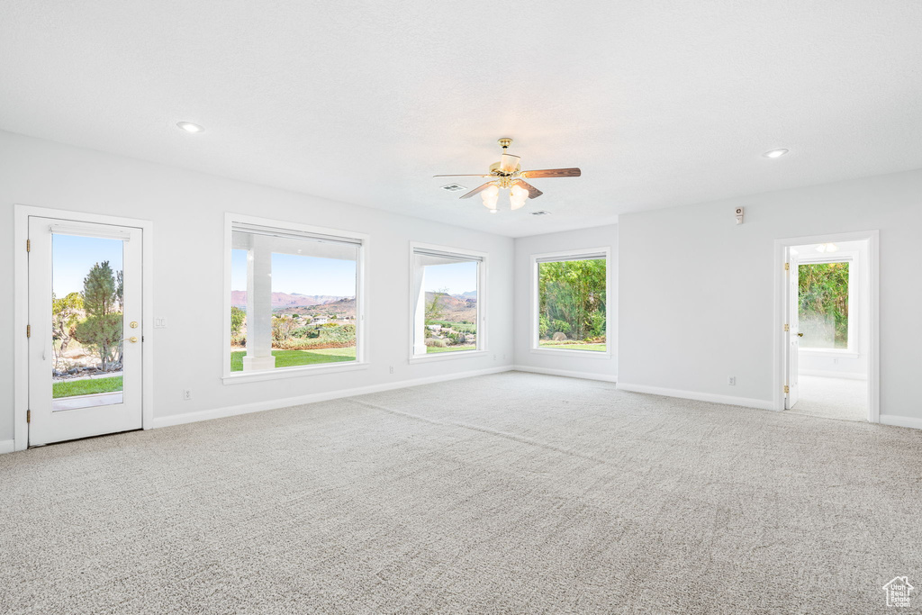 Carpeted spare room with ceiling fan and a healthy amount of sunlight