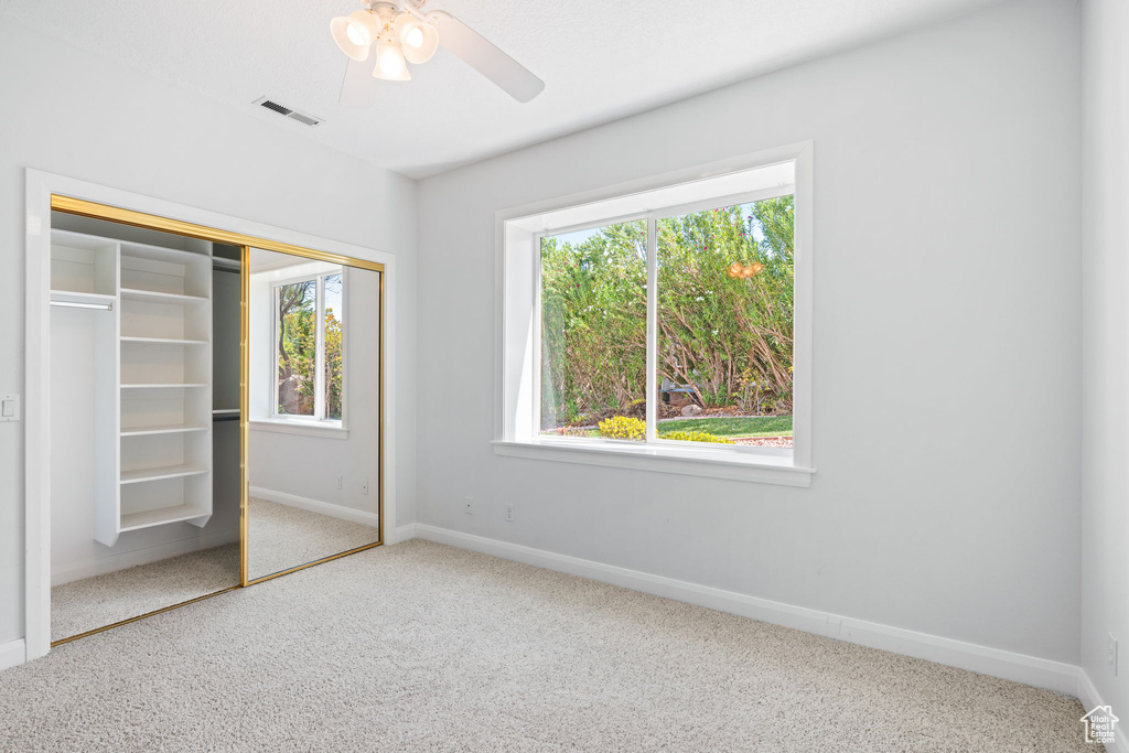 Unfurnished bedroom featuring ceiling fan, a closet, multiple windows, and carpet