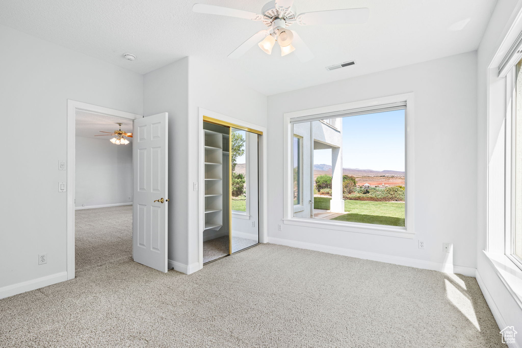 Unfurnished bedroom with ceiling fan, light colored carpet, multiple windows, and a closet