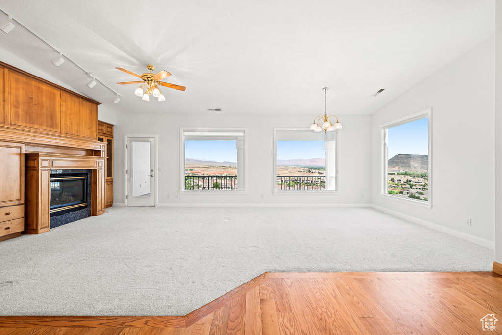 Unfurnished living room with ceiling fan with notable chandelier, track lighting, and light colored carpet