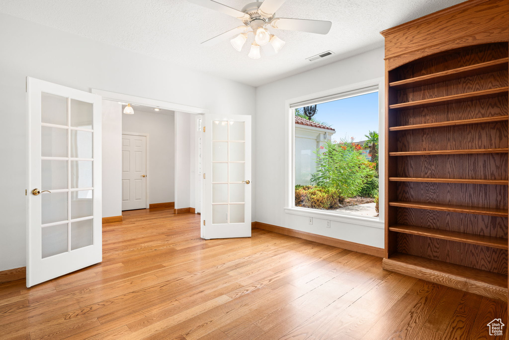 Empty room with french doors, a textured ceiling, light wood-type flooring, and ceiling fan