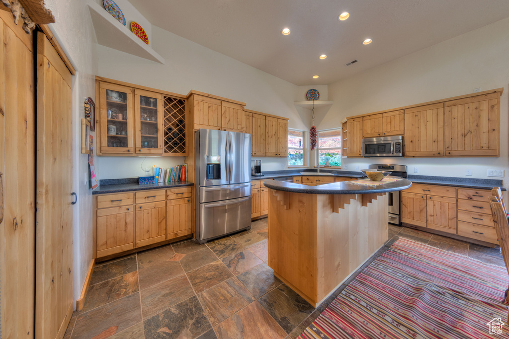 Kitchen featuring dark tile patterned floors, hanging light fixtures, a high ceiling, stainless steel appliances, and a kitchen island