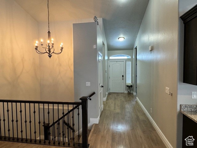 Hall with a chandelier, wood finished floors, an upstairs landing, and baseboards