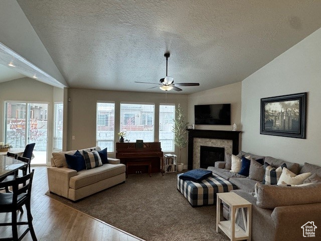 Living area featuring ceiling fan, a textured ceiling, wood finished floors, a high end fireplace, and vaulted ceiling