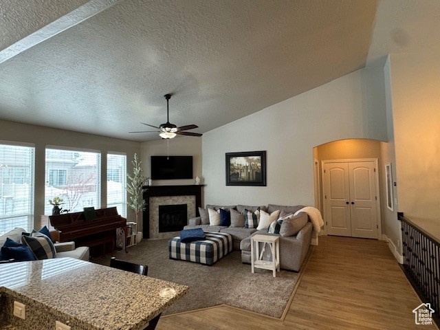 Living room with a fireplace, a ceiling fan, vaulted ceiling, a textured ceiling, and wood finished floors