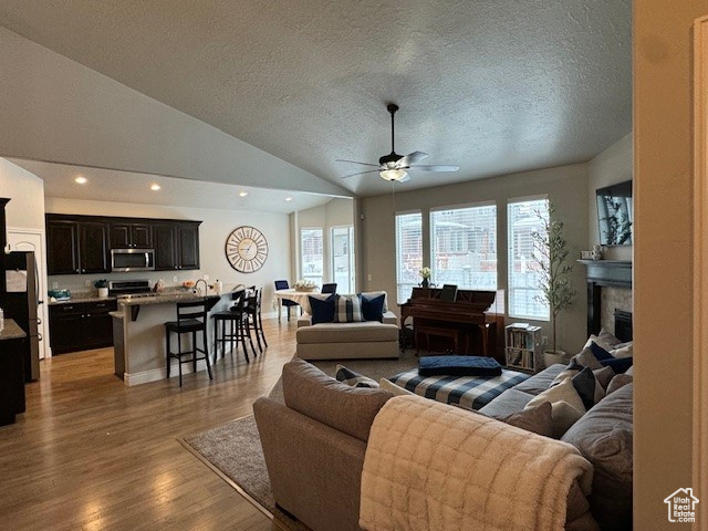 Living room featuring ceiling fan, recessed lighting, a fireplace, vaulted ceiling, and light wood finished floors