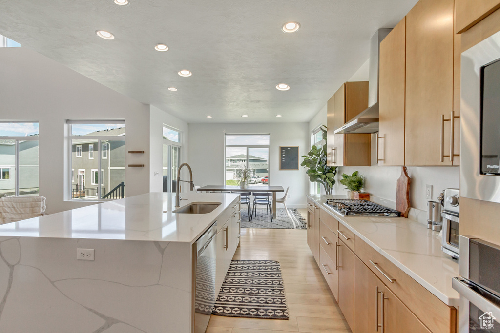 Kitchen featuring a center island with sink, light wood-type flooring, stainless steel appliances, light brown cabinetry, and sink