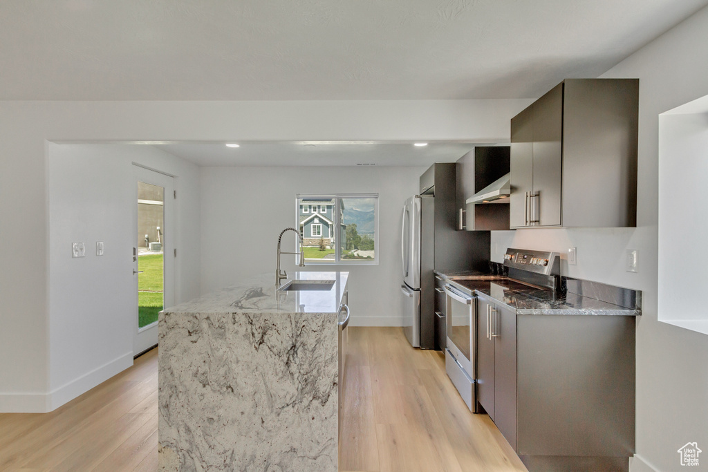 Kitchen with appliances with stainless steel finishes, sink, light stone countertops, and light hardwood / wood-style floors